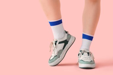 Spor ayakkabılı kadın bacakları ve pembe arka planda çoraplar.