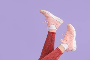 Leylak arka planında pembe spor ayakkabılı kadın bacakları