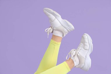 Leylak arka planında beyaz spor ayakkabılı kadın bacakları