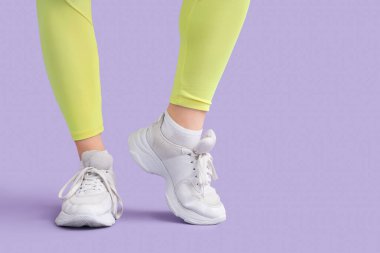 Leylak arka planında beyaz spor ayakkabılı kadın bacakları