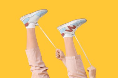 Sarı arka planda ayakkabı bağcıkları bağlayan genç kadın.