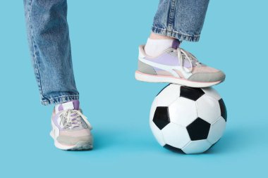 Şık spor ayakkabılı kadın bacakları ve mavi arka planda futbol topu olan kot pantolonlar.