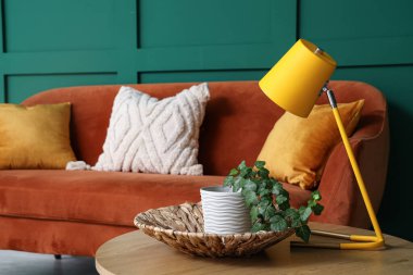 Kahverengi kanepe ve kahve masası lambası yeşil duvarın yanında.