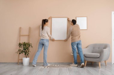 Evdeki bej duvarda boş bir çerçeve asılı genç bir çift.