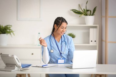 Klinikteki masada dizüstü bilgisayarla çalışan genç Afro-Amerikalı kadın doktor.