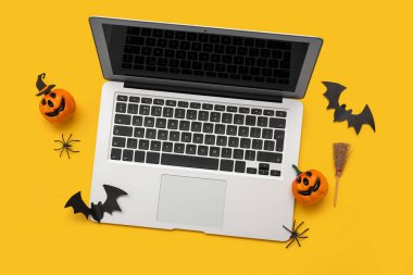 Sarı arka planda Cadılar Bayramı için modern dizüstü bilgisayar ve dekor kompozisyonu