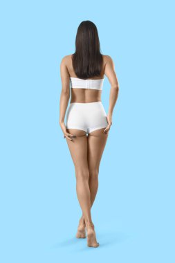 Mavi arka planda selülit sorunu olan iç çamaşırlı genç bir kadın.