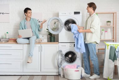 Dizüstü bilgisayarı olan erkek öğrenciler yatakhanede çamaşır yıkıyorlar.