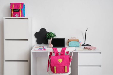 Okul malzemeleri, dizüstü bilgisayar ve sırt çantalarının bulunduğu çalışma alanı beyaz duvarın yanında.