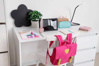 Okul malzemeleri, dizüstü bilgisayar ve sırt çantalı çalışma alanı beyaz duvarın yanında.