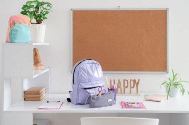 Okul gereçleri, tahta ve sırt çantalı çalışma alanı beyaz duvarın yanında.