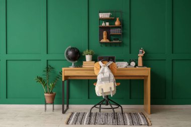 Okul malzemeleri, dizüstü bilgisayar ve sırt çantalı çalışma alanı yeşil duvarın yanında.