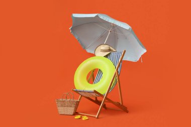 Güverte sandalyesi, plaj şemsiyesi, şapka, hasır çanta, parmak arası terlik ve kırmızı arka planda şişme yüzük.