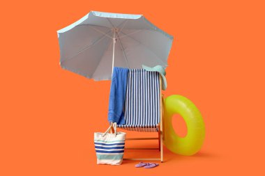Güverte sandalyesi, plaj şemsiyesi, şapka, çanta, havlu, parmak arası terlik ve kırmızı arka planda şişme yüzük.