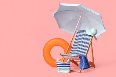 Güverte sandalyesi, plaj şemsiyesi, havlu, şapka, çanta ve pembe arka planda şişme yüzük.
