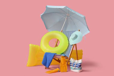 Güverte sandalyesi, plaj şemsiyesi, şapka, çanta, palet, havlu, şişirilebilir yatak ve pembe arka planda yüzük.