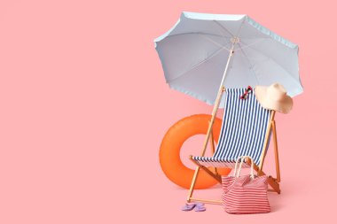 Güverte sandalyesi, plaj şemsiyesi, çanta, şapka, parmak arası terlik, güneş gözlüğü ve pembe arka planda şişme yüzük.