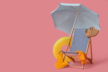 Güverte sandalyesi, plaj şemsiyesi, çanta, şapka, parmak arası terlik, güneş gözlüğü ve pembe arka planda şişme yüzük.