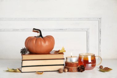 Dekoratif balkabağı, sonbahar yaprakları, kitaplar ve çay fincanı ışık duvarının yanındaki masada.