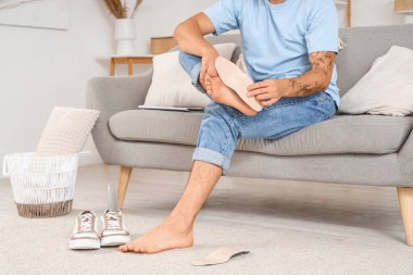 Düz tabanlı genç adam evdeki kanepeye ortopedik taban takıyor.