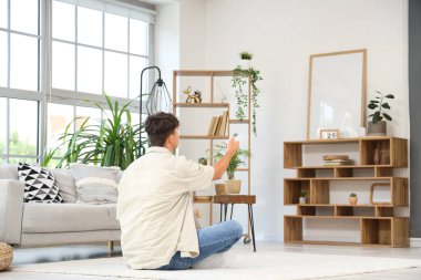 Yakışıklı genç adam evde yerde klimayı çeviriyor, arkadan bakıyor.