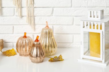 Sonbahar yapraklı dekoratif balkabakları ve beyaz tuğla duvarın yanındaki rafta duran fener.