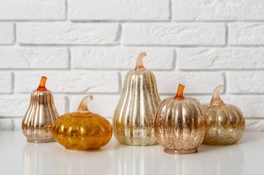 Rafta beyaz tuğla duvarın yanında dekoratif balkabakları var.