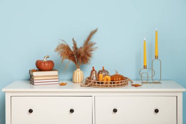 Mumları yanan dekoratif balkabakları, otlar ve mavi duvarın yanındaki klozette bulunan kitaplar.