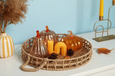 Süslü balkabağı tepsisi, köknar kozalakları ve mavi duvarın yanındaki rafta yanan mum.