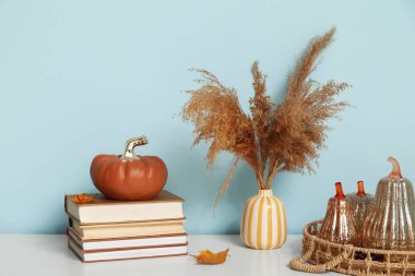 Çimenli vazolar, dekoratif balkabakları, sonbahar yaprakları ve mavi duvarın yanındaki raflarda kitaplar.