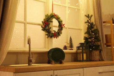 Geceleri mutfağın penceresinde parlayan ışıklar olan Noel çelengi.