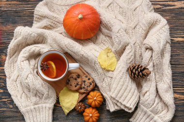 Bir fincan çay, sıcak süveter, mumlar ve koyu ahşap arka planda sonbahar dekoru ile kompozisyon