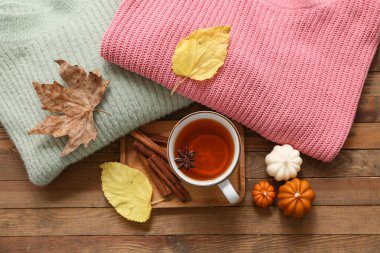 Ahşap arka planda çay, kazak, mum ve sonbahar yapraklı kompozisyon