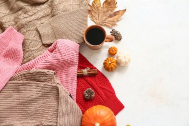 Şık kadın kazakları, bir fincan kahve ve açık arkaplanda sonbahar dekoru olan kompozisyon