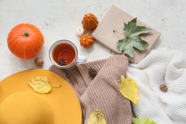 Kadın süveter, şapka, bir fincan çay ve arka planda sonbahar dekoru olan kompozisyon