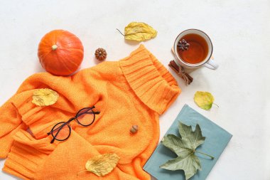 Süslü, sıcak süveter, kitap, bir fincan çay ve arka planda sonbahar dekoru olan kompozisyon