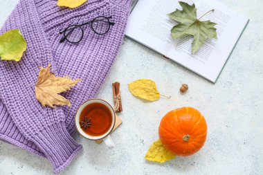 Örgü süveter, kitap, çay fincanı ve açık arkaplanda sonbahar yapraklarıyla kompozisyon