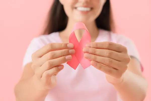 stock image Young woman with pink ribbon on color background, closeup. Breast cancer awareness concept