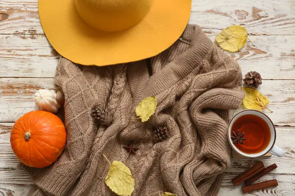 A steaming cup of pine needle tea with fresh pine needles scattered around it on a rustic wooden table.