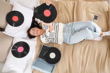Plakçalar için vinil diskleri olan güzel bir kadın. Yatakta uzanıyor.