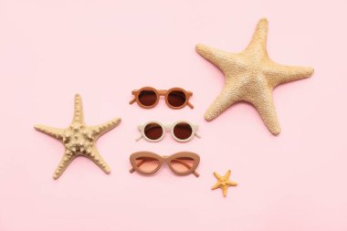 Farklı tarz güneş gözlükleri ve pembe arka planda deniz yıldızları.