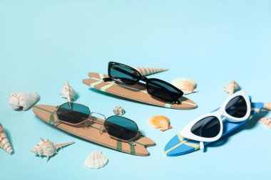 Sörf tahtaları ve mavi arka planda deniz kabukları olan farklı stil güneş gözlükleri.