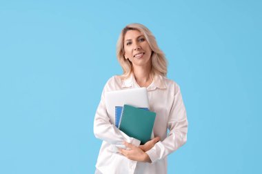 Dizüstü bilgisayarı ve mavi arka planda defterleri olan güzel bir iş kadını.