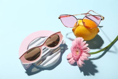 Süslü güneş gözlüklü dekoratif podyumlar, mavi arka planda taze limon ve gerbera çiçeği