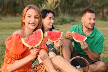 Bir dilim karpuzla genç bir kadın ve arkadaşları gün batımında parkta piknik yapıyorlar.