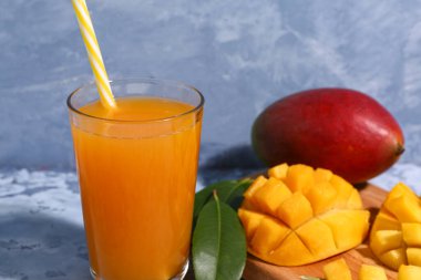 Mavi arka planda bir bardak taze mango smoothie, yakın plan.
