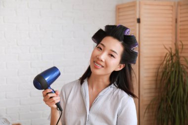 Güzel Asyalı bir kadın banyoda saçlarını kurutuyor.