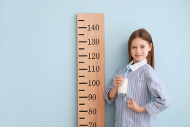 Açık mavi arka planda bir bardak sütü ve stadyumu olan küçük bir kız.