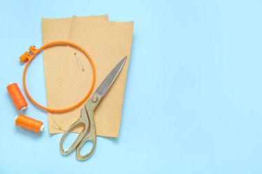 Mavi arka planda tuval, makas ve iplik makaralı nakış çemberi