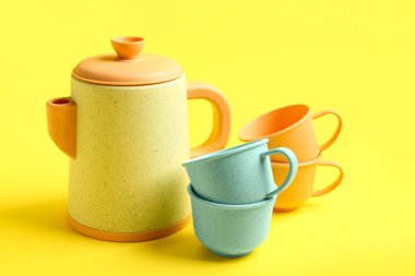 Sarı arka planda bebek için fincanları olan çaydanlık